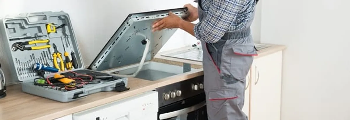 Cooktop repair technician lifting a built-in stovetop for service in Manchester, NH