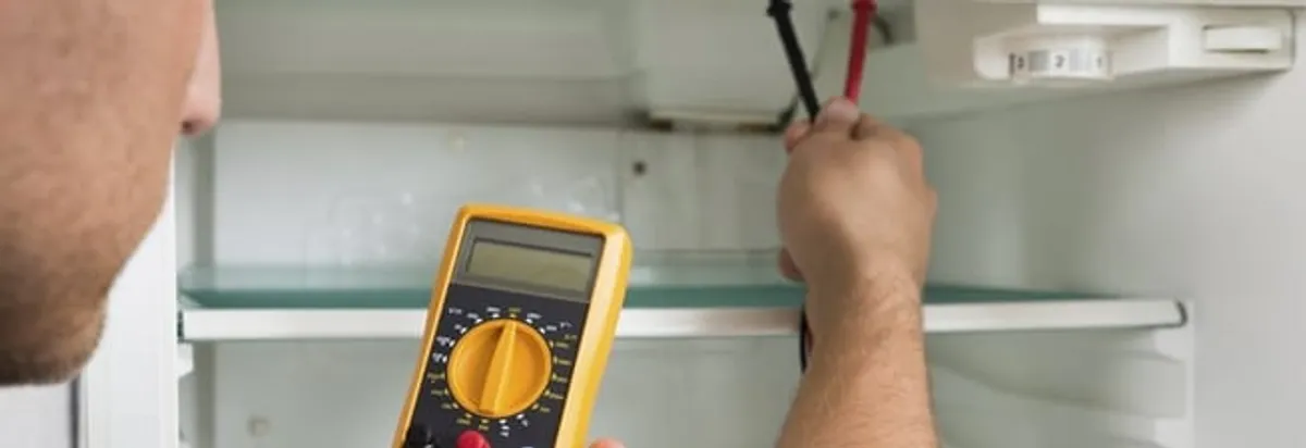 Refrigerator repair technician testing electrical components with a multimeter in Manchester, NH