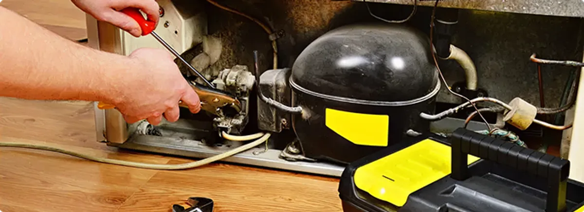 Refrigerator repair technician fixing the compressor and wiring in Manchester, NH